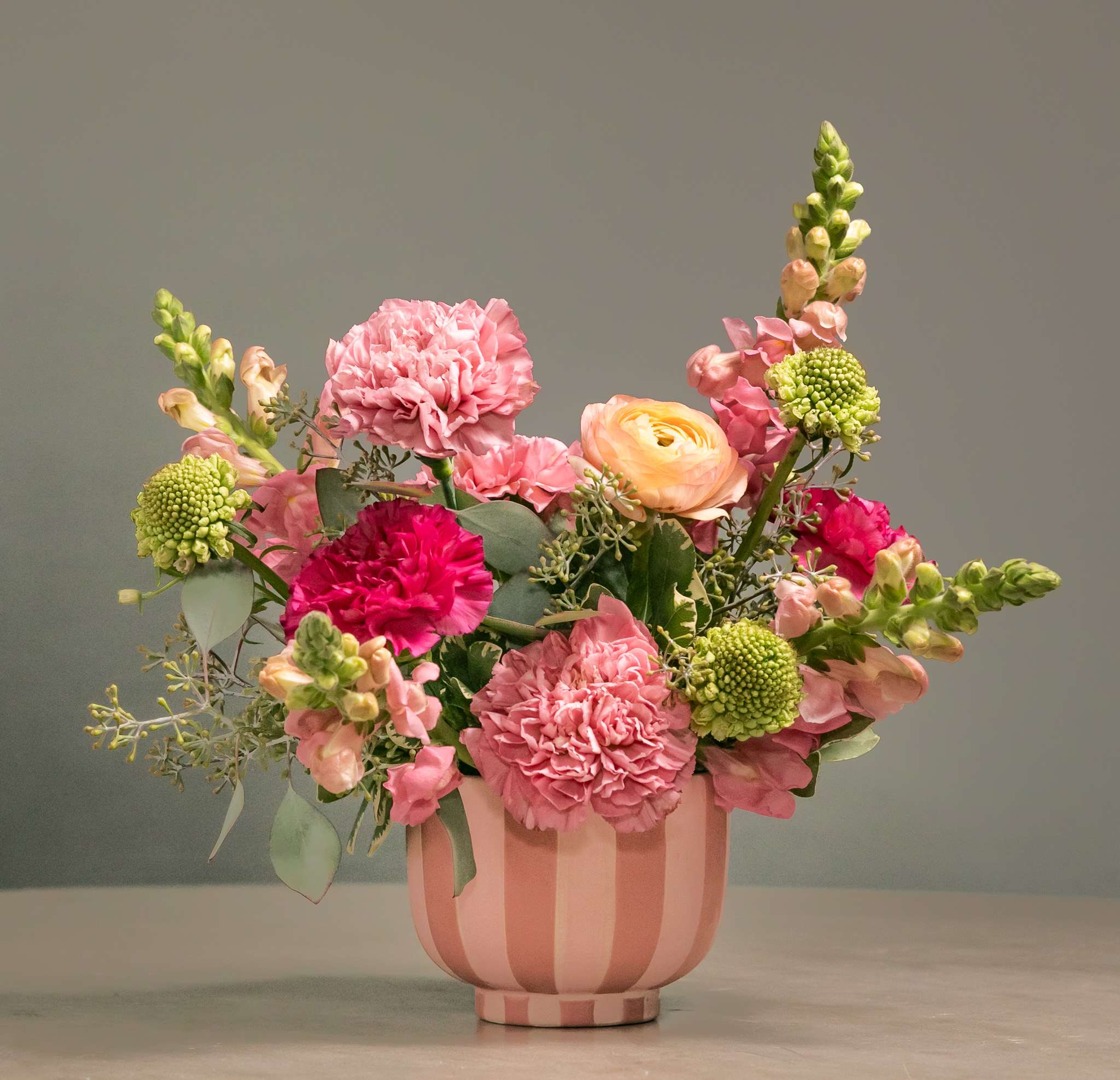Pink and peach mixed flower arrangement in a striped pink vase
