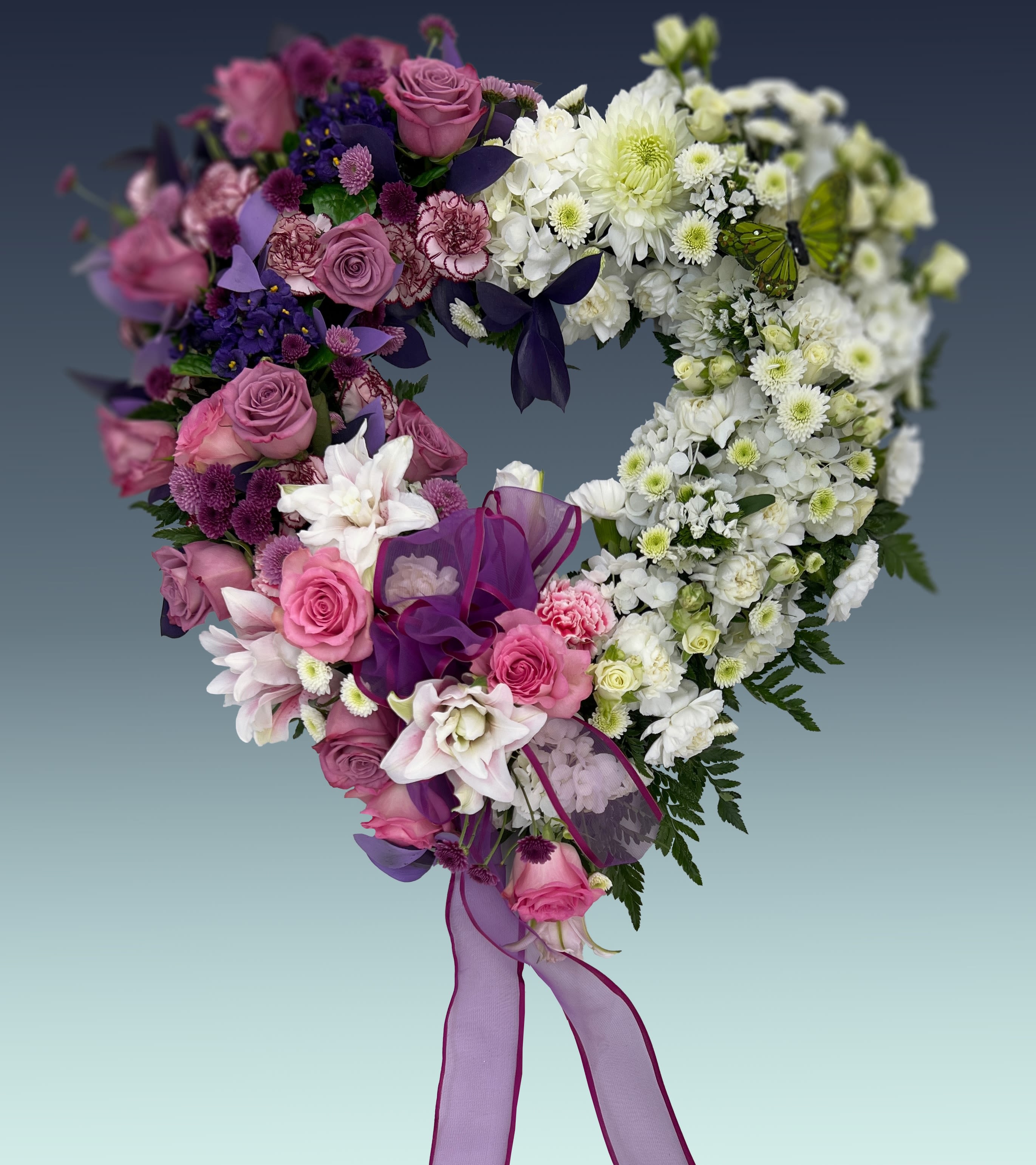 Beloved Heart - *Premium depicted*   A tender and deeply comforting tribute, the Beloved Heart standing spray is thoughtfully designed to express your deepest condolences, enduring love, and reverence. This beautifully crafted open-heart arrangement features a soft, elegant palette of delicate pinks, serene whites, and soothing lavender tones, bringing a sense of peace and warmth to funeral services, wakes, or celebrations of life.  Our expert designers meticulously hand-arrange dense clusters of premium chrysanthemums and lush hydrangeas, beautifully accented by the elegant textures of ruffled lisianthus and exquisite phalaenopsis orchids. Mounted securely on a traditional display easel, this breathtaking floral display stands as a beautiful testament to a life well-lived and a bond that will never be forgotten. Size range: 19"-23".   Looking to personalize this piece? We are happy to tailor the colors, flower selections, or size to match your vision perfectly. For custom requests or dedicated assistance, please call us directly at 305.769.3843.