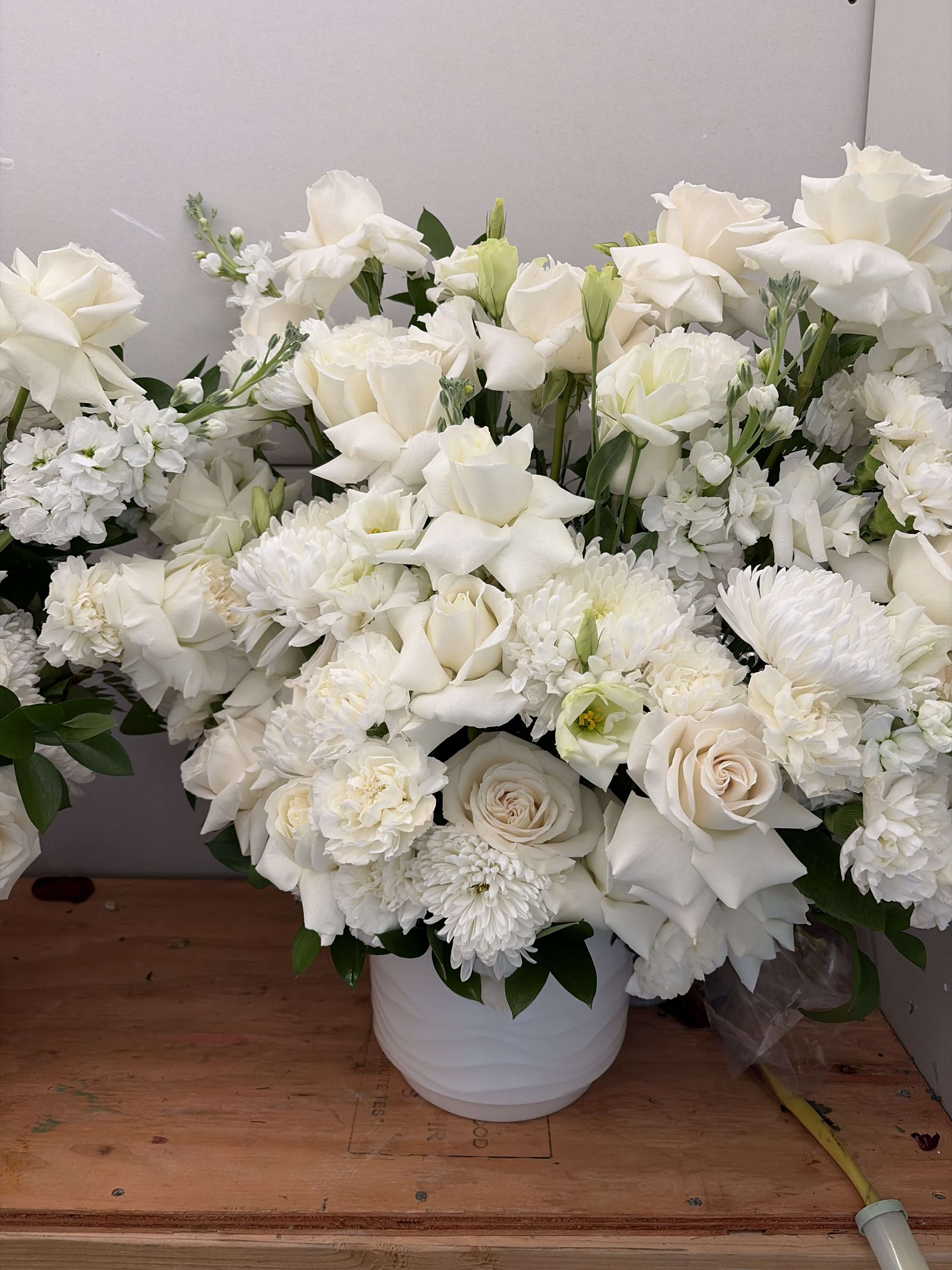 White floral arrangement in a white vase with roses, lilies, and mums