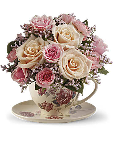 Pink and cream roses arranged in a floral teacup with saucer