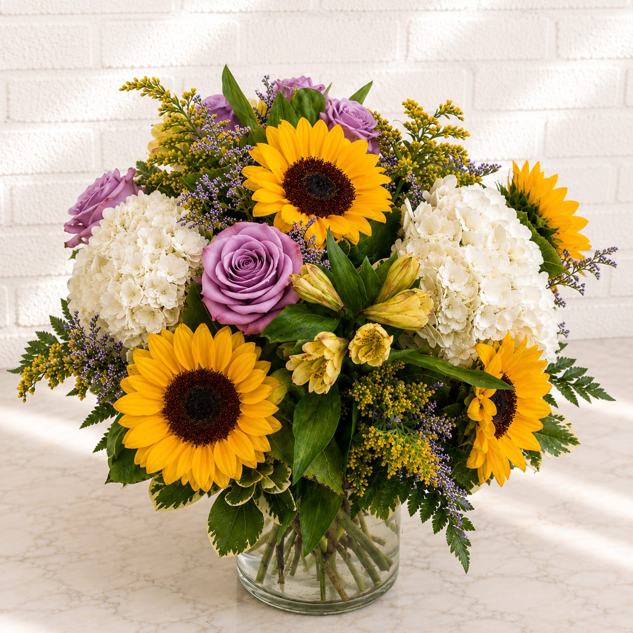 Bouquet of sunflowers, lavender roses, and white hydrangeas in a glass vase