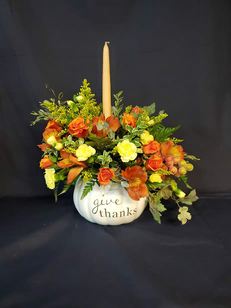 Orange and yellow floral arrangement in a white pumpkin container with a candle