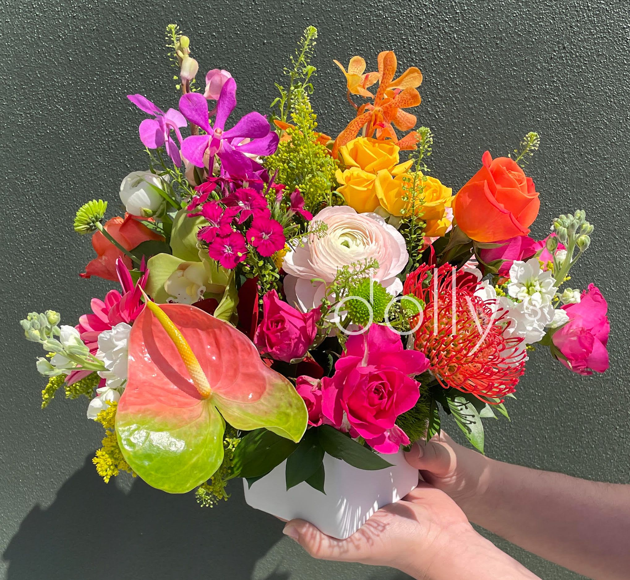 Bright mixed arrangement of pink, yellow, and orange flowers in a white cube vase.