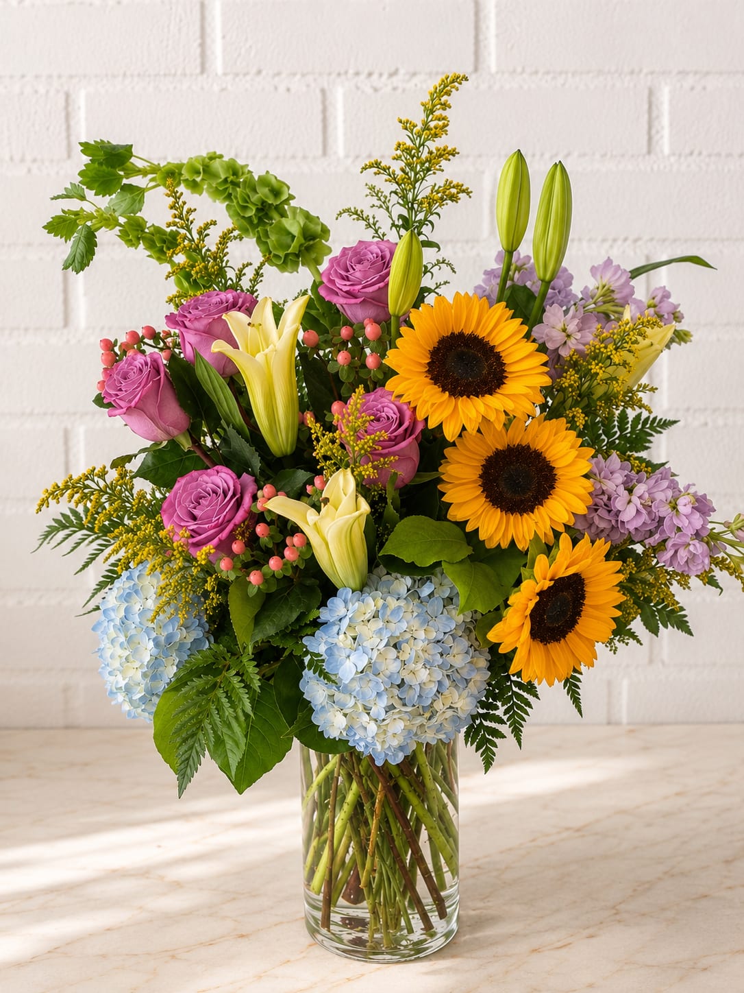 Mixed bouquet with sunflowers, roses, lilies, and hydrangeas in a glass vase