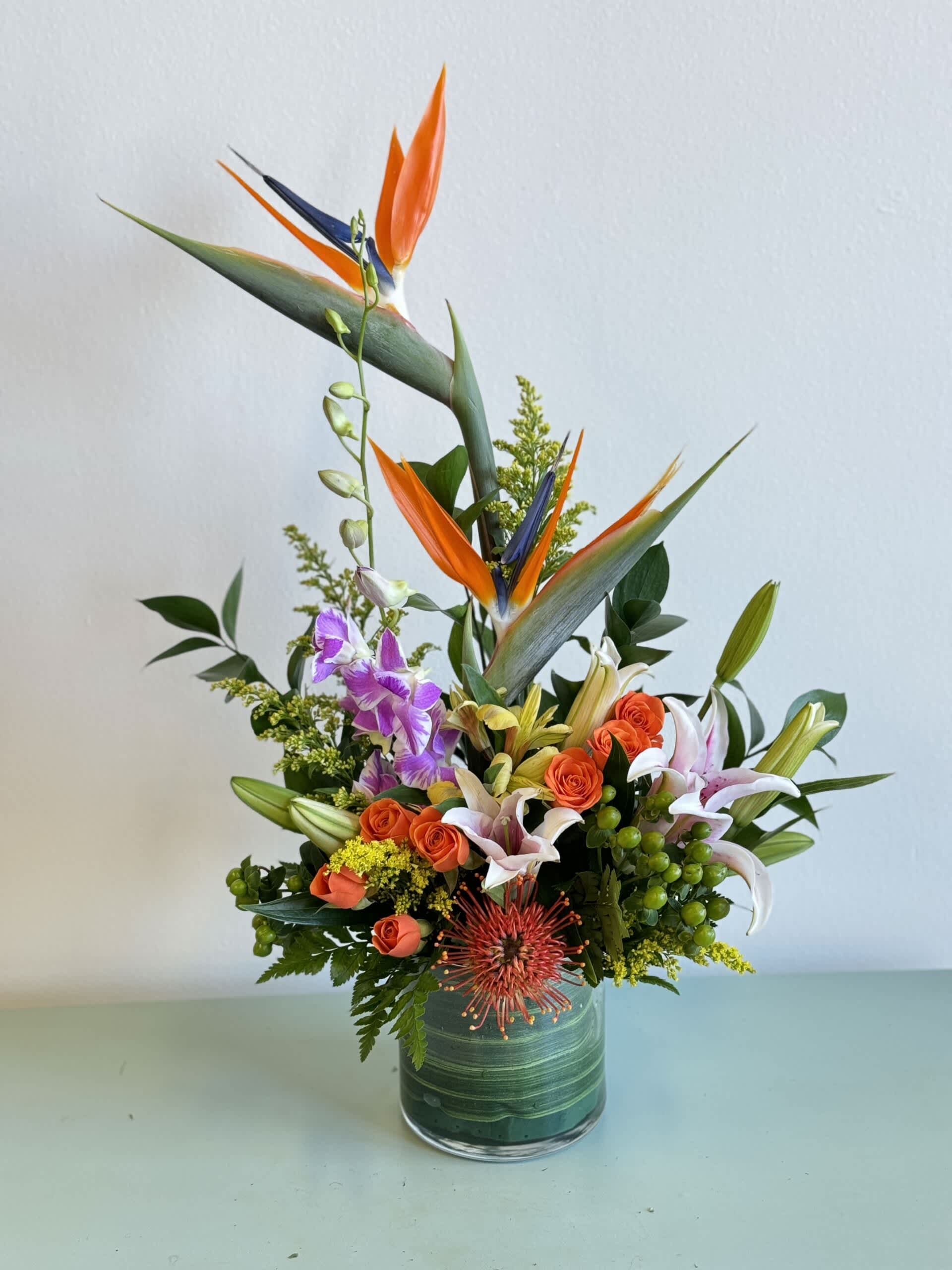 Tropical bouquet with orange bird of paradise and lilies in a glass vase