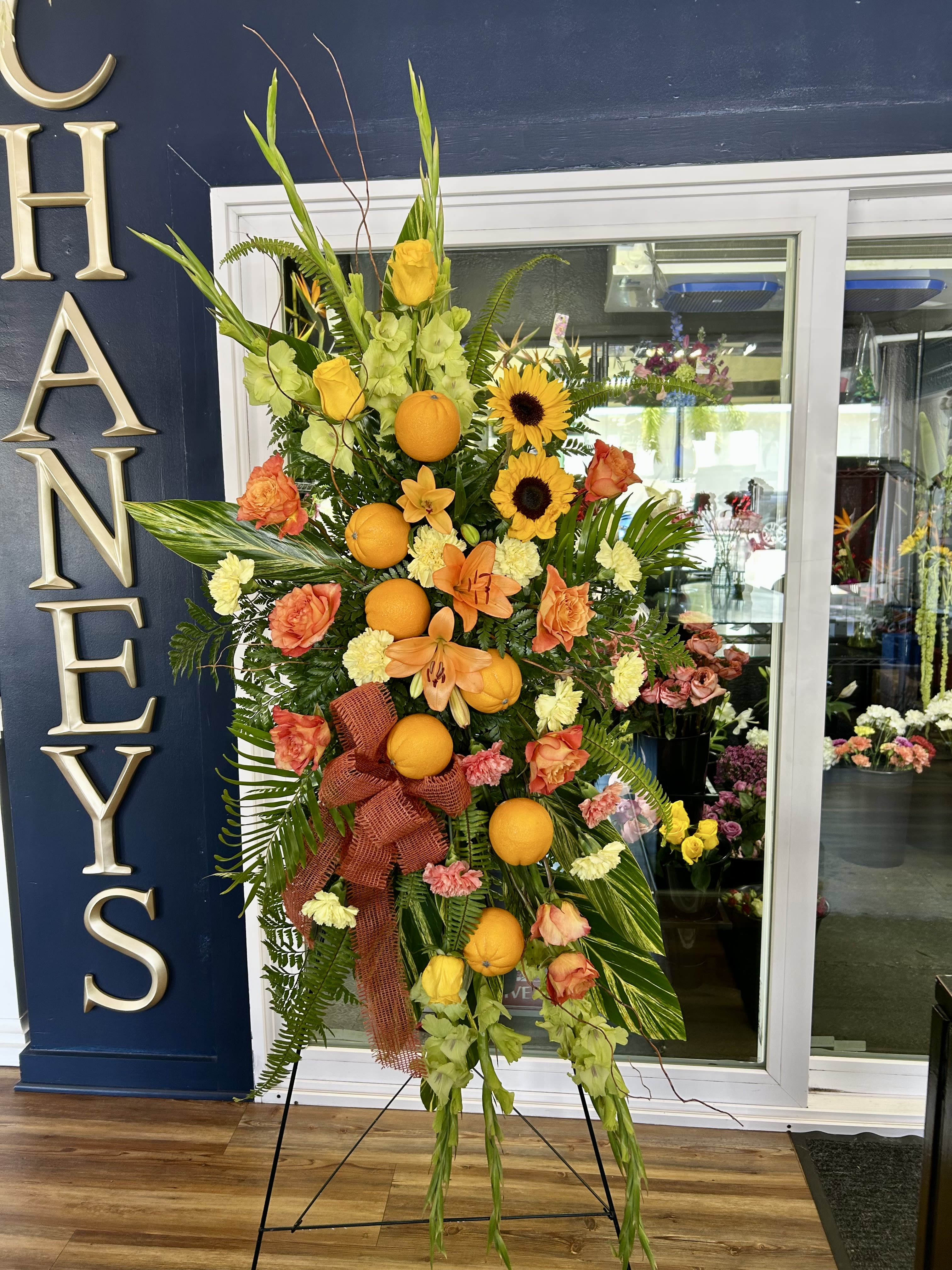 Tall floral standing spray with oranges, sunflowers, and peach roses
