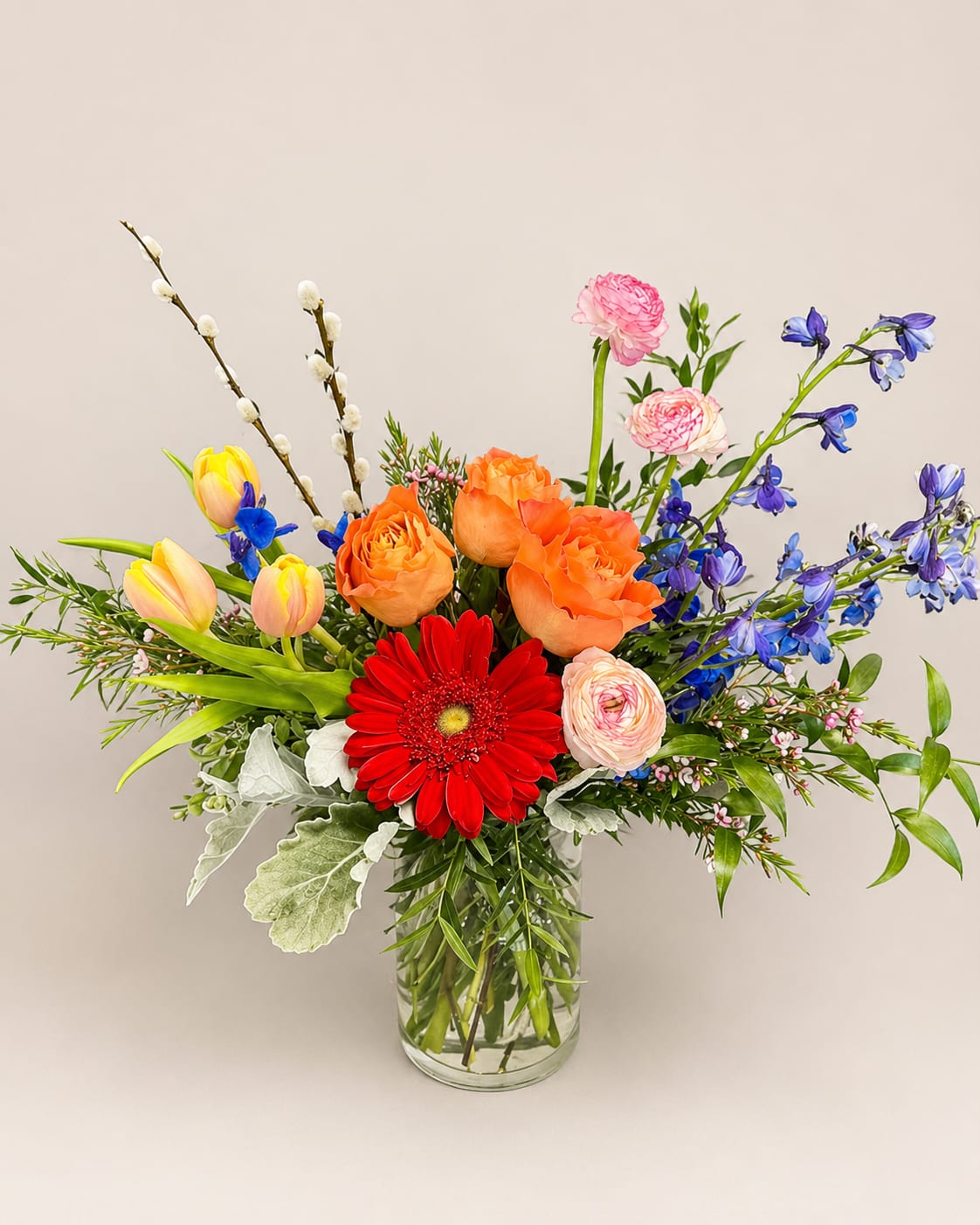 Mixed bouquet in a clear glass vase with orange, red, pink, yellow, and blue flowers