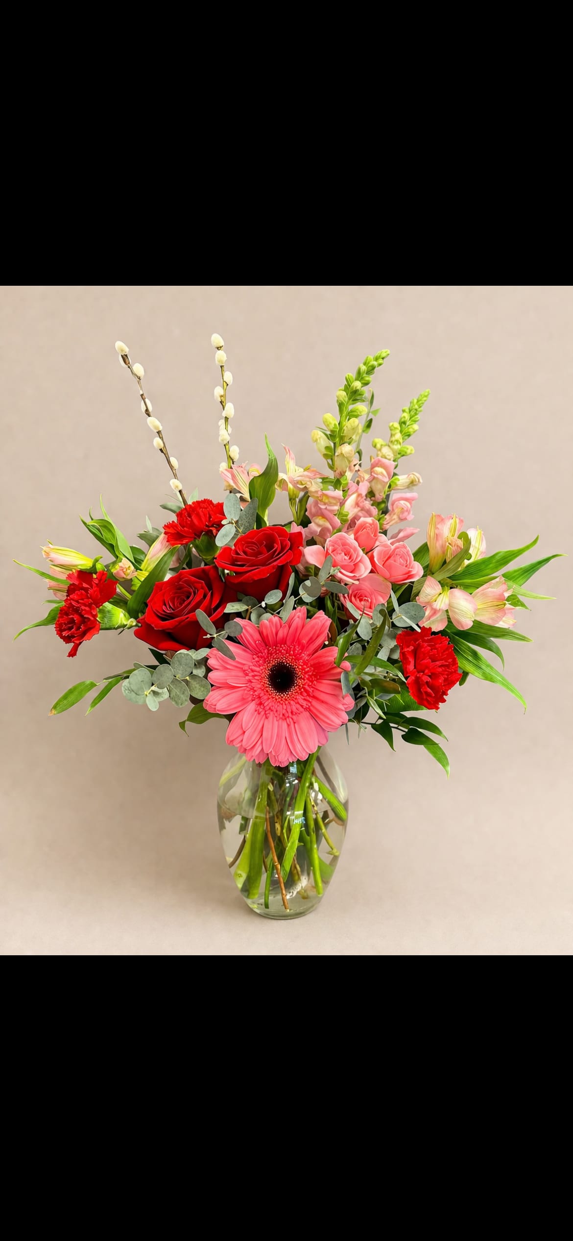Mixed bouquet with red roses, pink gerberas, and carnations in a glass vase