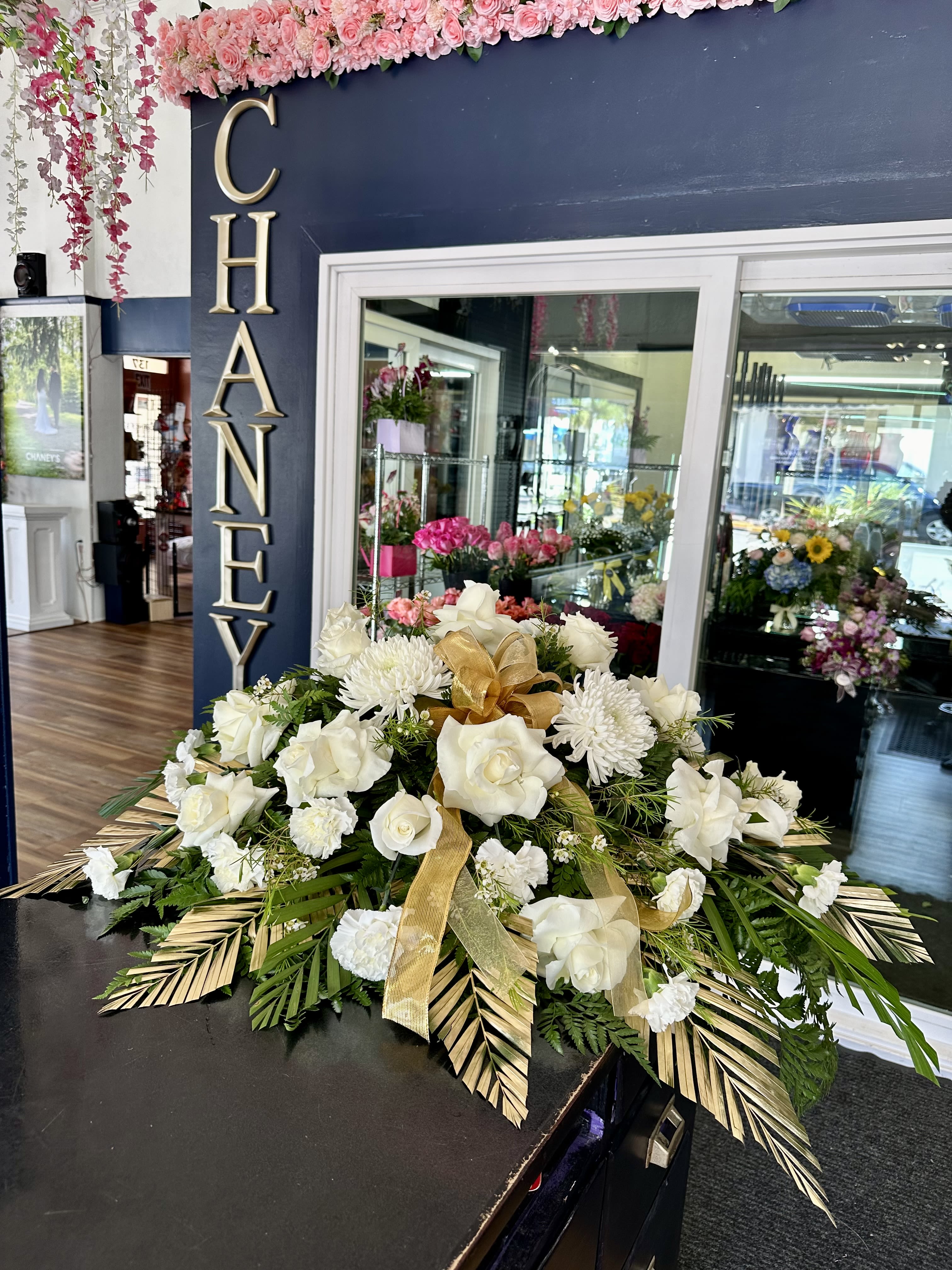 White floral arrangement with roses and chrysanthemums, accented by gold ribbon