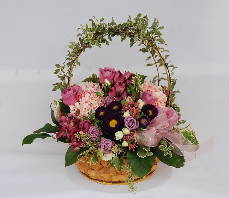 Basket arrangement of pink and purple flowers with a ribbon and arch handle