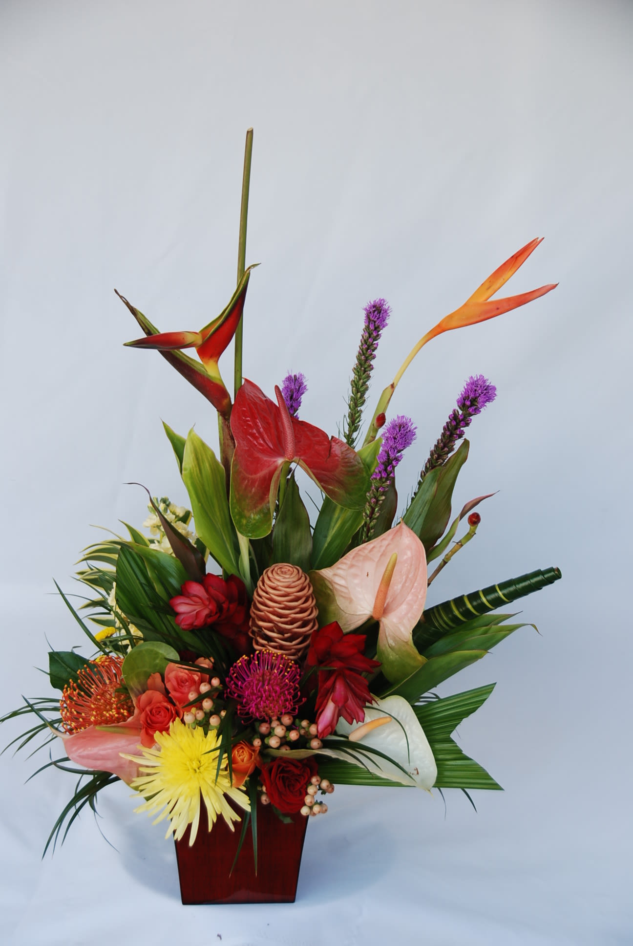 Tropical flower arrangement in a red vase with anthuriums and orchids