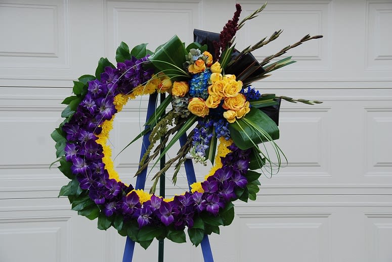 Purple and yellow floral wreath on an easel with roses and orchids
