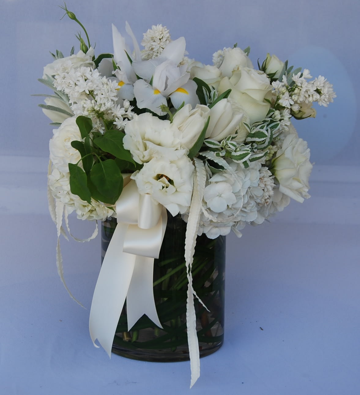 White floral arrangement in a dark glass vase with a satin ribbon