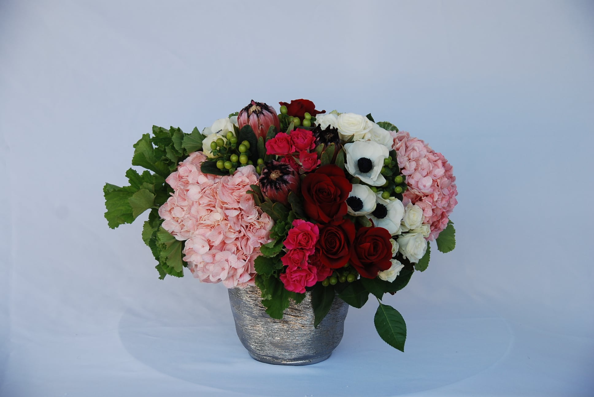 Mixed bouquet of roses, hydrangeas, and anemones in a silver vase
