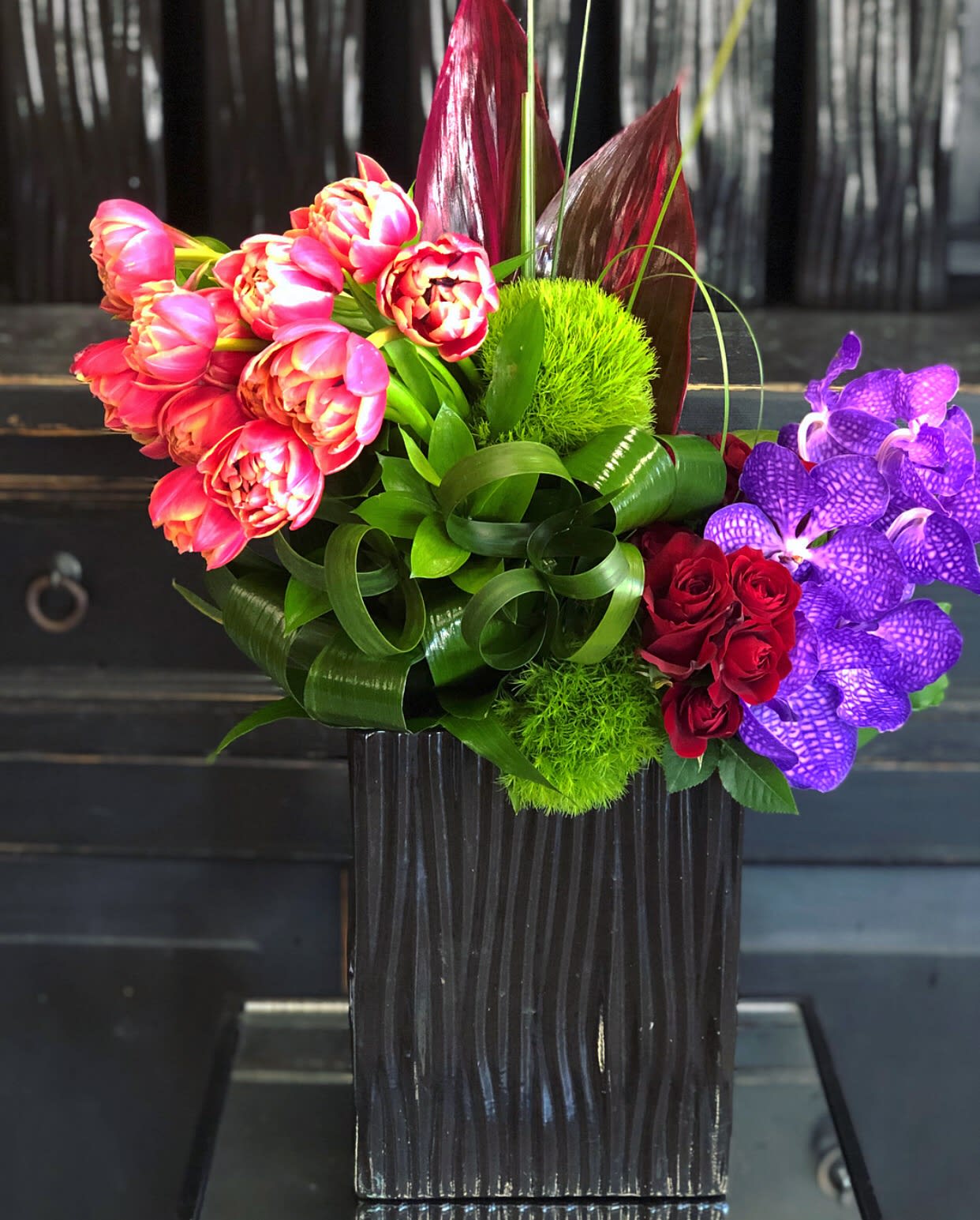 Colorful bouquet with tulips, roses, and purple orchids in a black vase