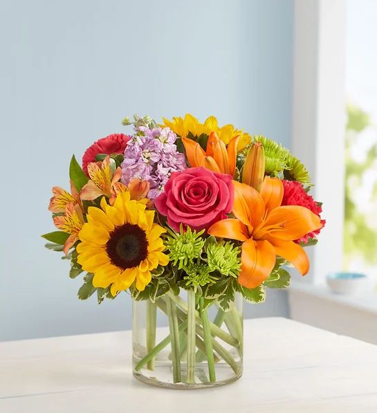 Mixed bouquet in a clear glass vase with a sunflower and orange lilies