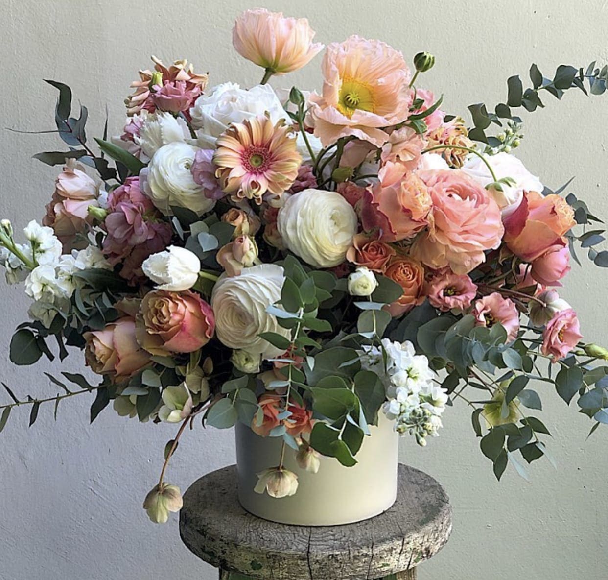 Mixed bouquet of peach, pink, and white flowers in a white vase