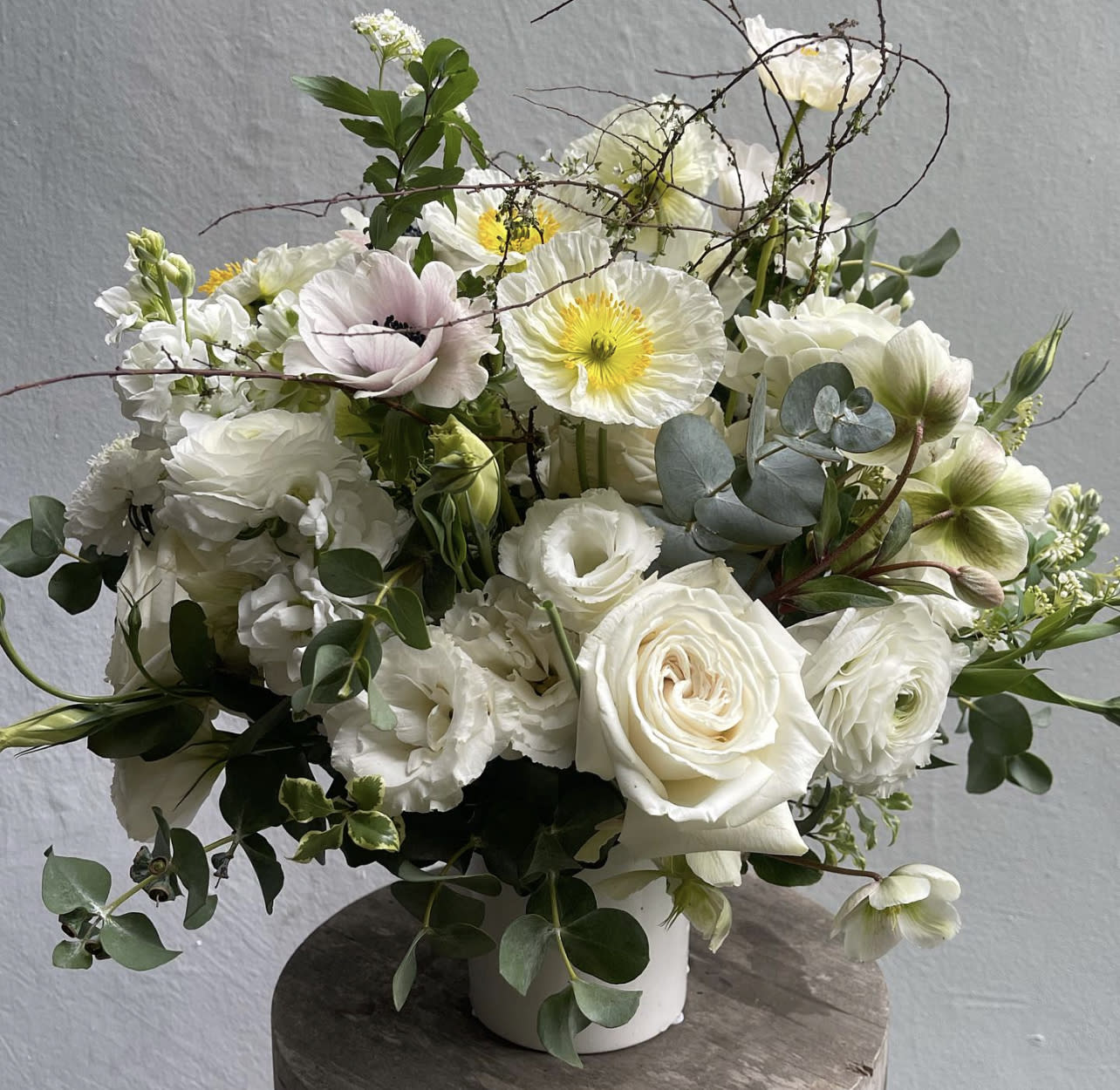 White floral arrangement in a white vase with roses and poppy-like blooms
