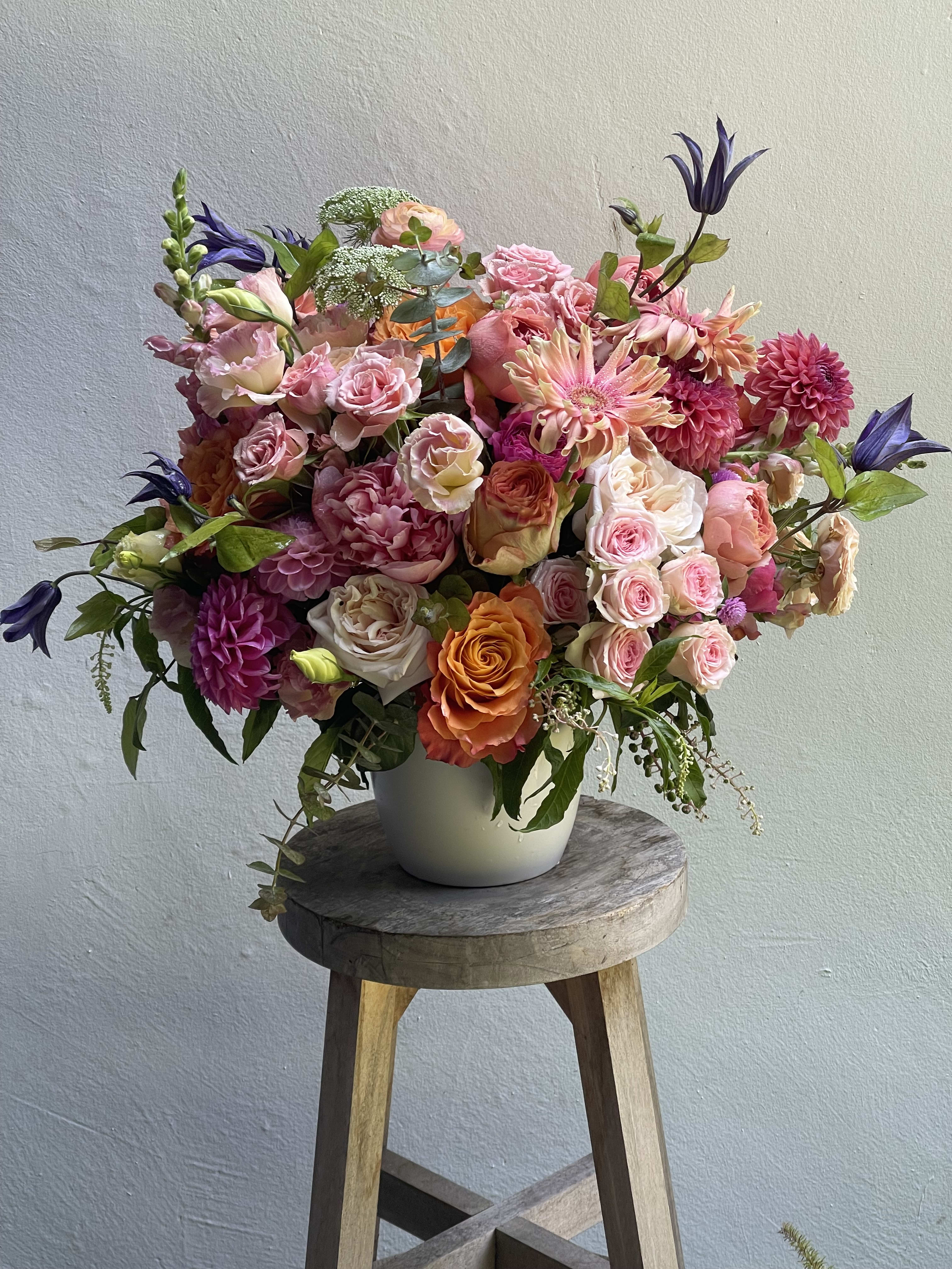 Large mixed bouquet of pink, peach, and purple flowers in a white vase
