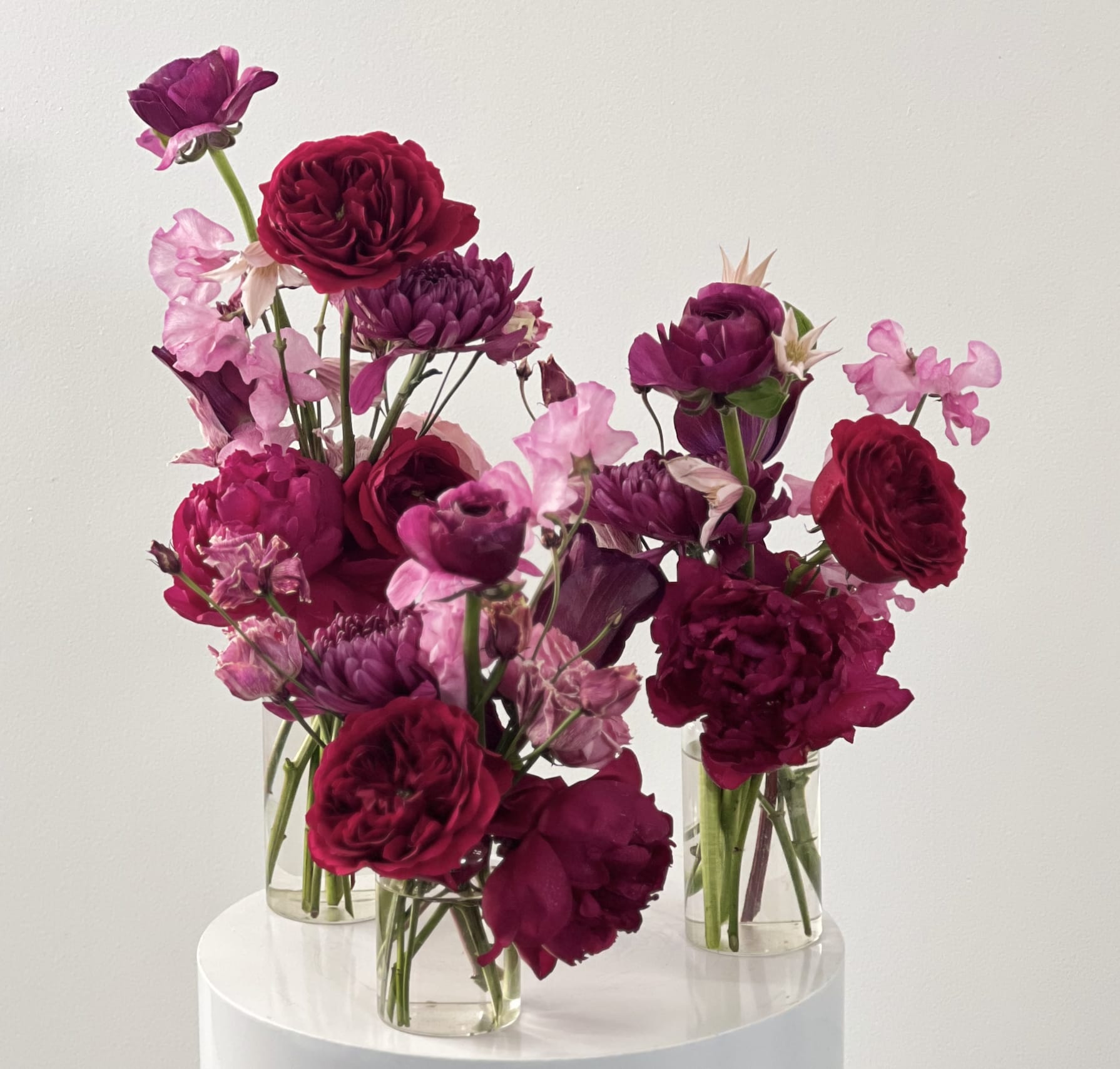 Three small glass vases hold magenta and pink flowers.