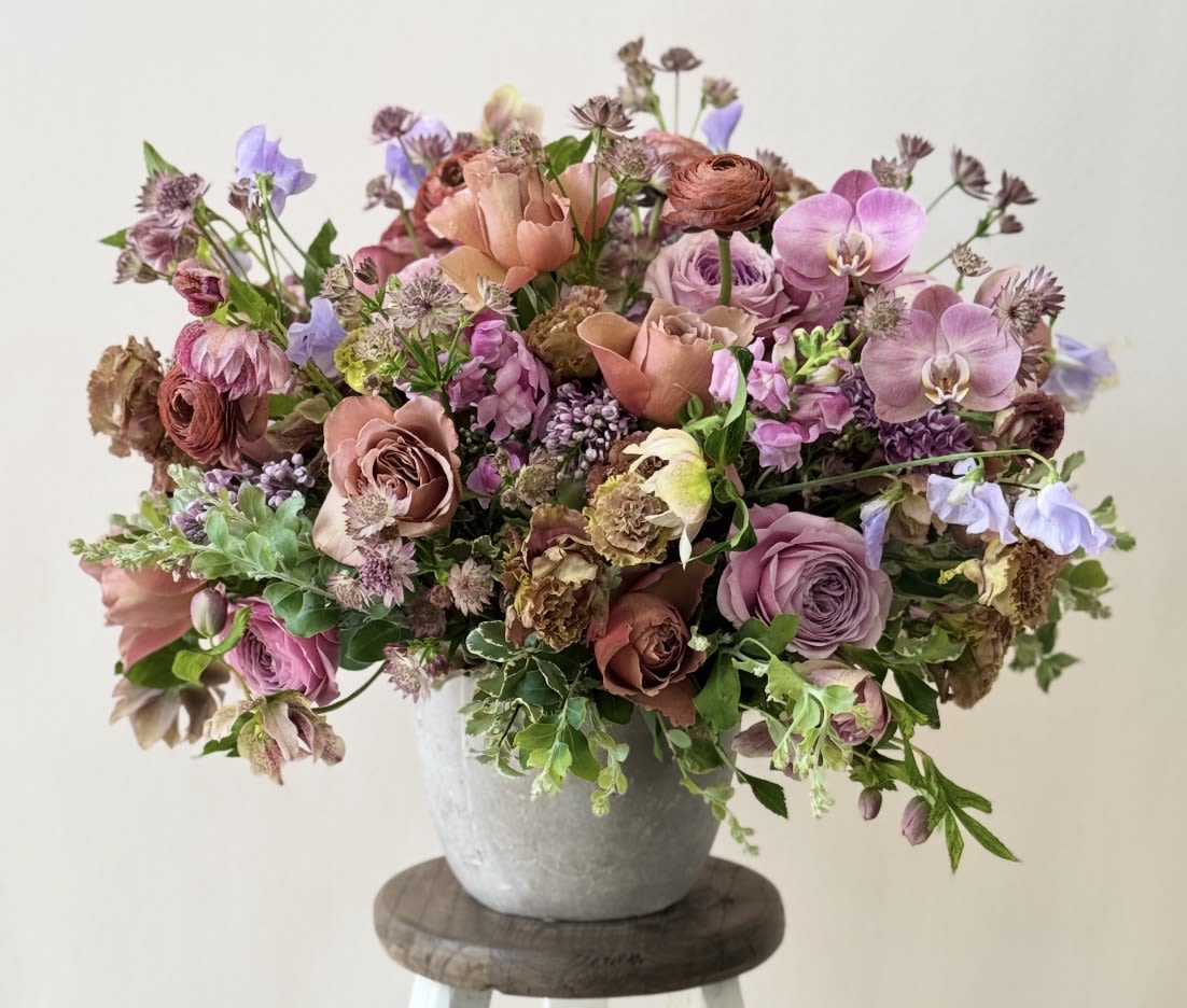 A mixed bouquet of pink, lavender, and peach flowers in a gray vase.