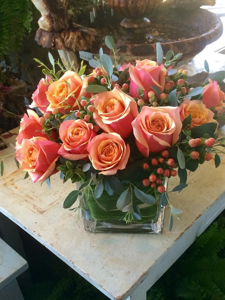 Low arrangement of peach and pink roses in a clear glass cube vase