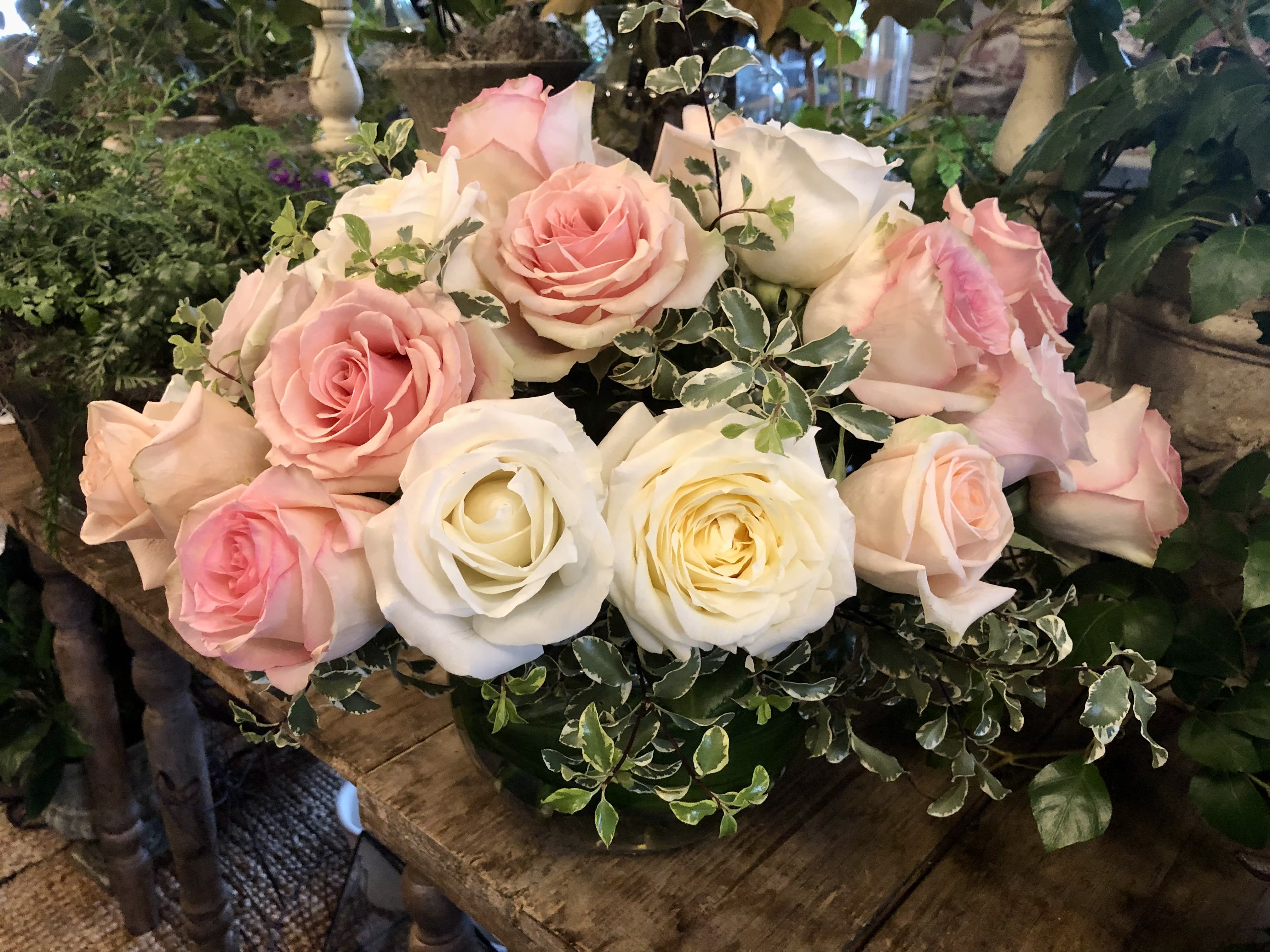 Low arrangement of pink and white roses with variegated foliage in a glass bowl vase