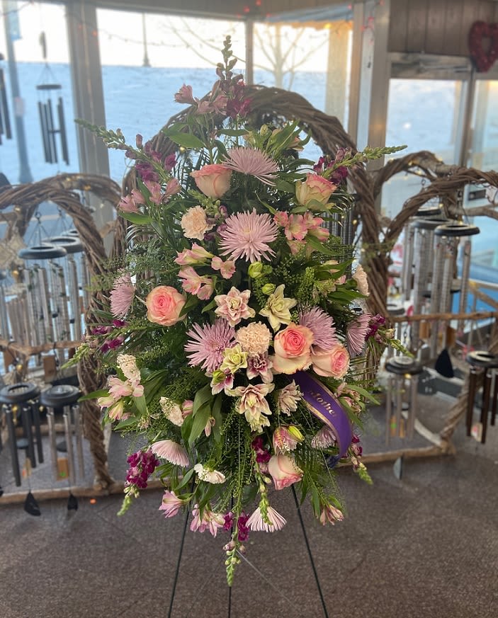 Standing spray of pink roses and mixed flowers on an easel with a purple ribbon