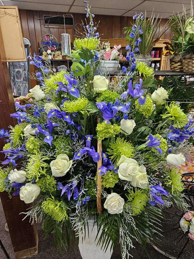 Tall blue iris, green mums, and white rose arrangement in a white pedestal vase