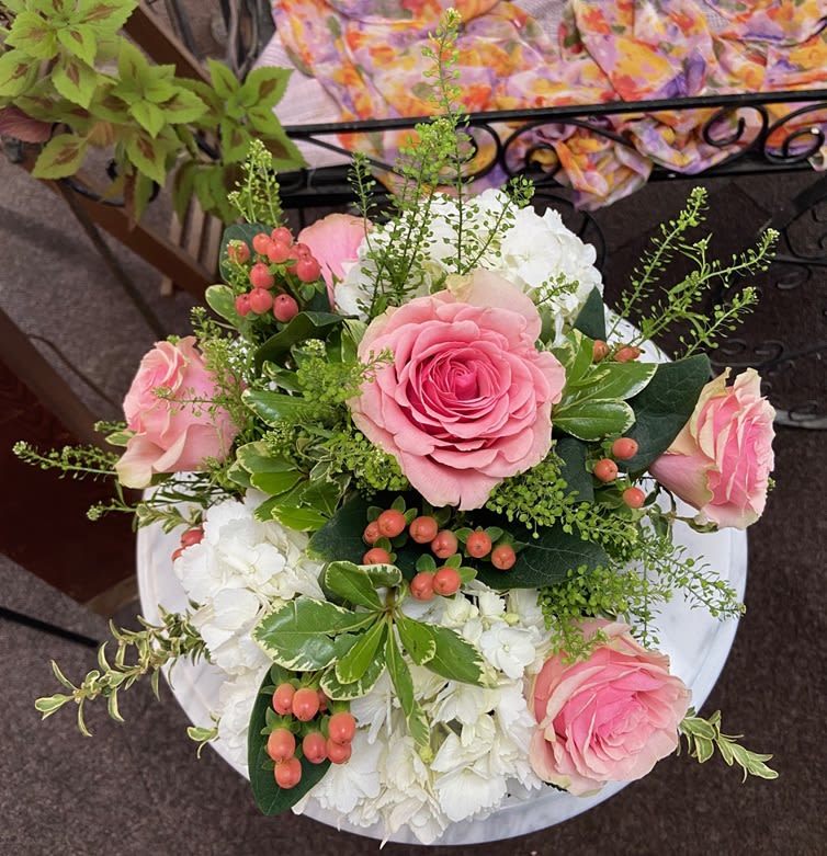 Round arrangement of pink roses with white hydrangeas and peach berries viewed from above.
