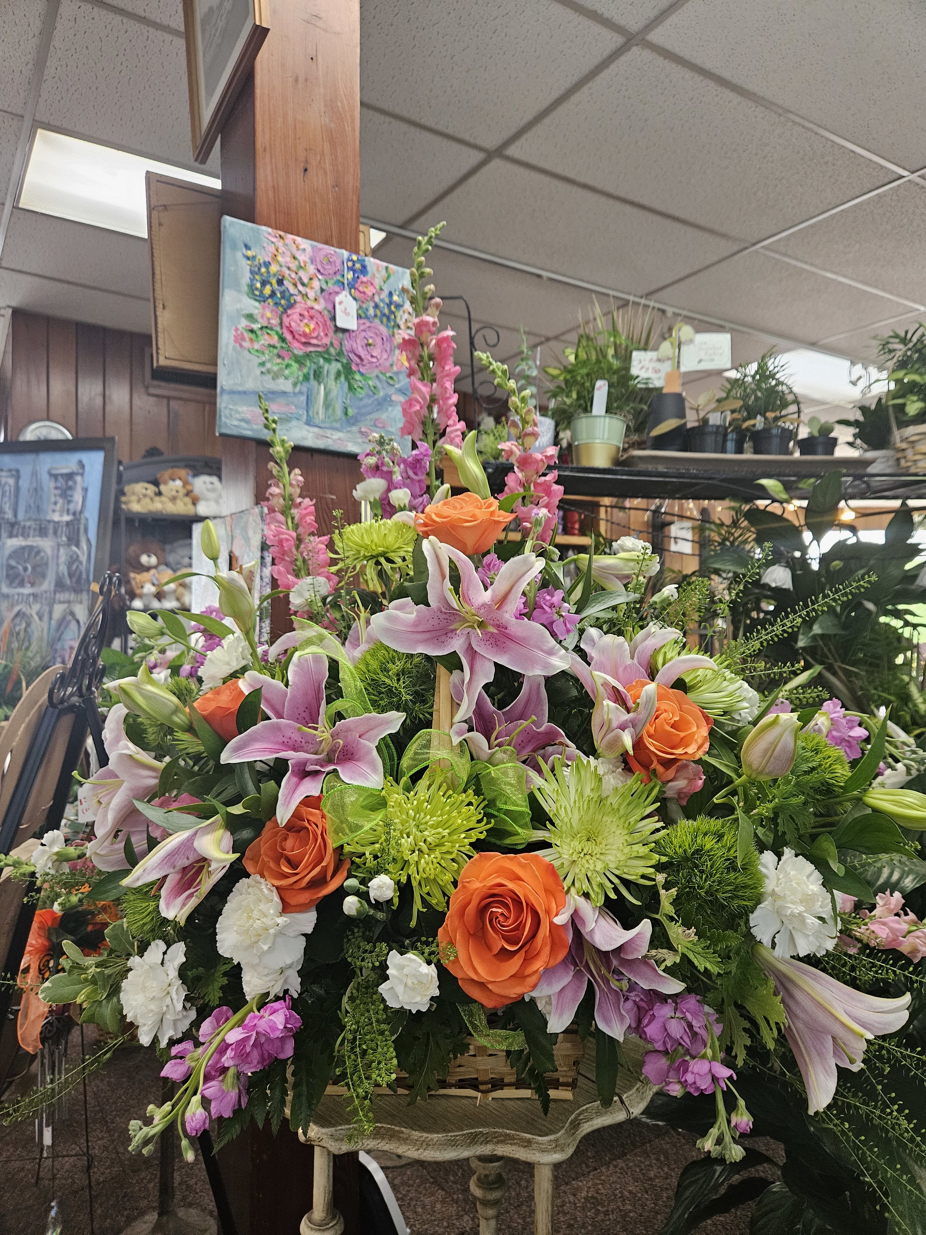 Large basket arrangement with pink lilies, orange roses, green mums, and white carnations on a small stand