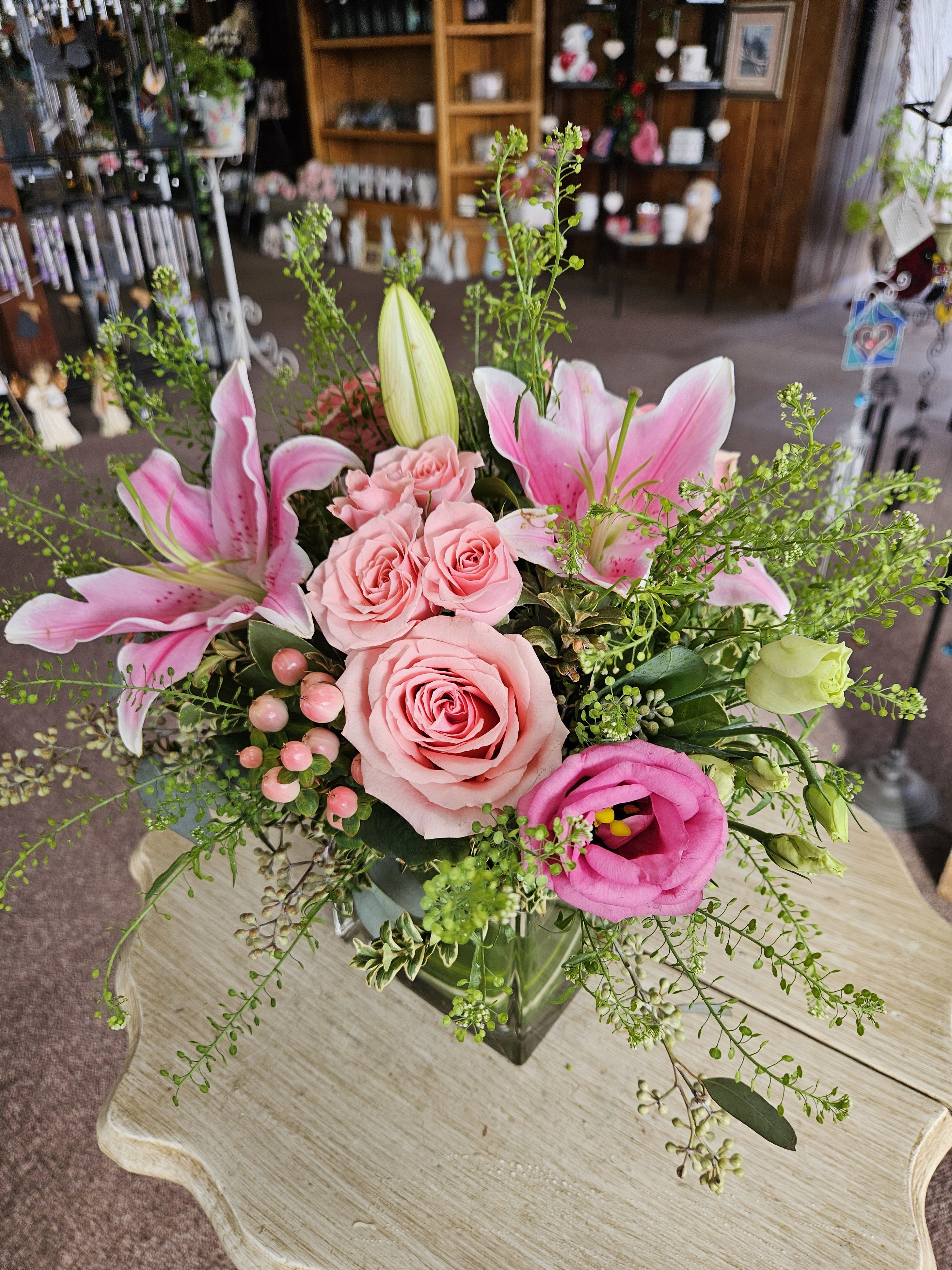 Pink lilies, roses, and lisianthus arranged in a clear glass cube vase