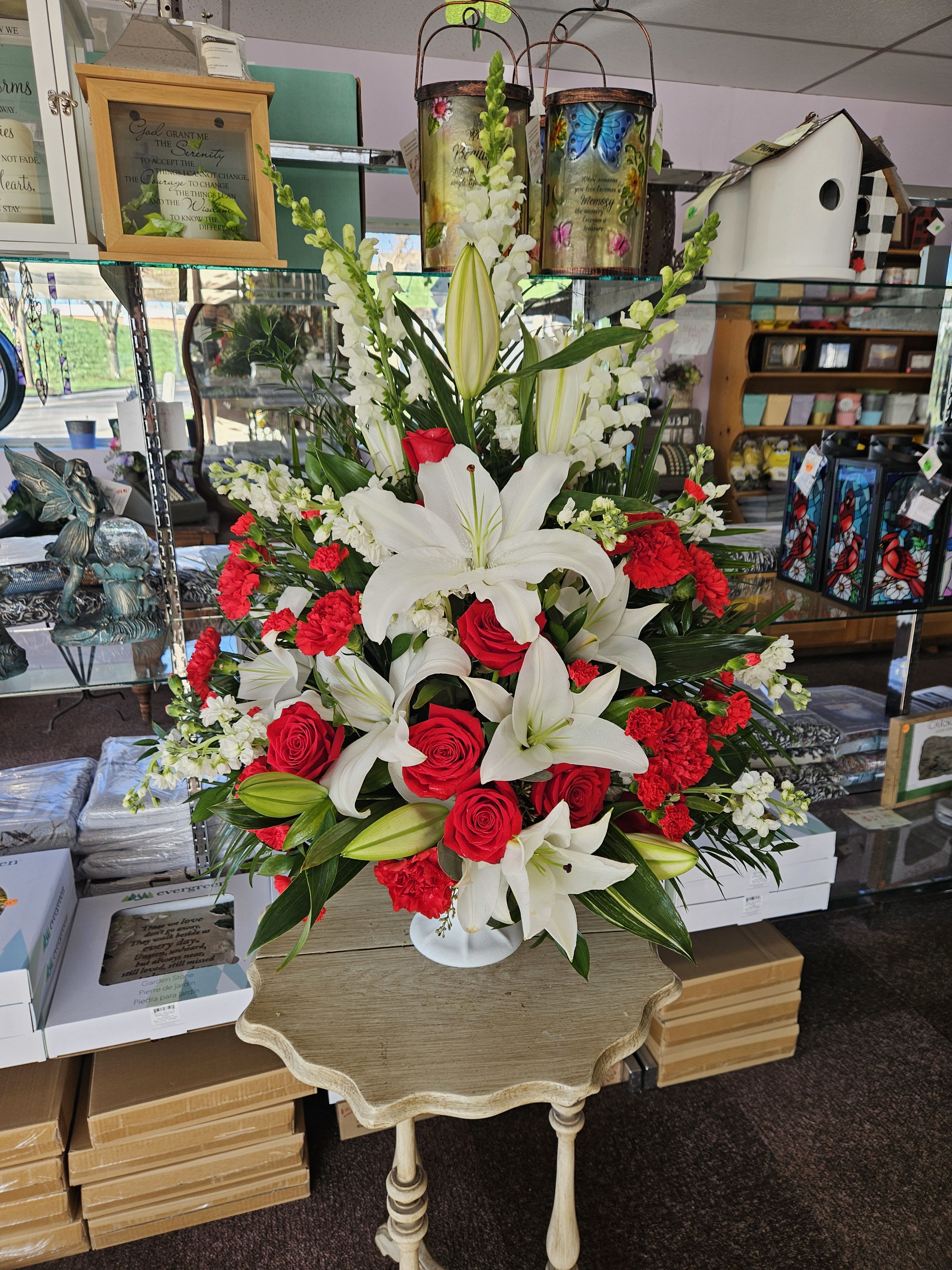 Tall arrangement of white lilies, red roses, red carnations, and white snapdragons in a white pedestal vase