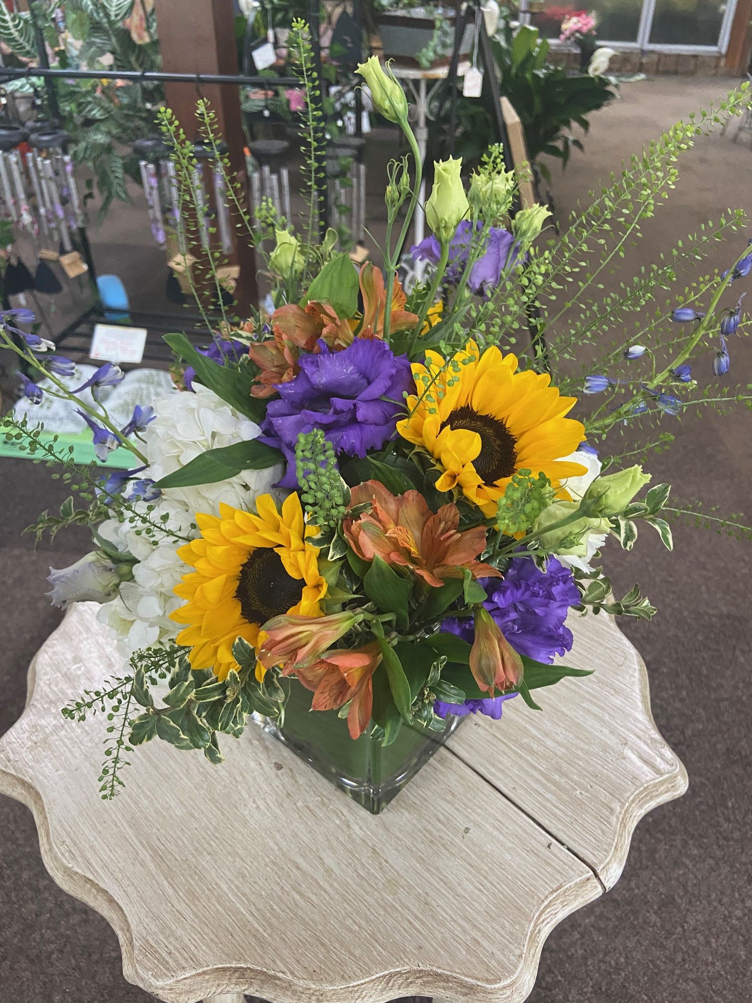 Summer Sweetness - Sweetness roses, purple lisianthus, fluffy white hydrangeas, piercing blue delphinium, and yellow peruvian lilies arranged in a leaf lined square cube.