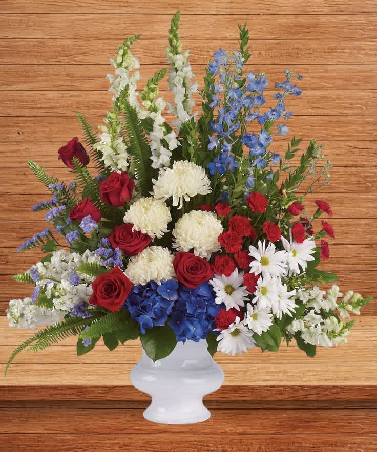 Red roses, white daisies, and blue flowers in a white vase