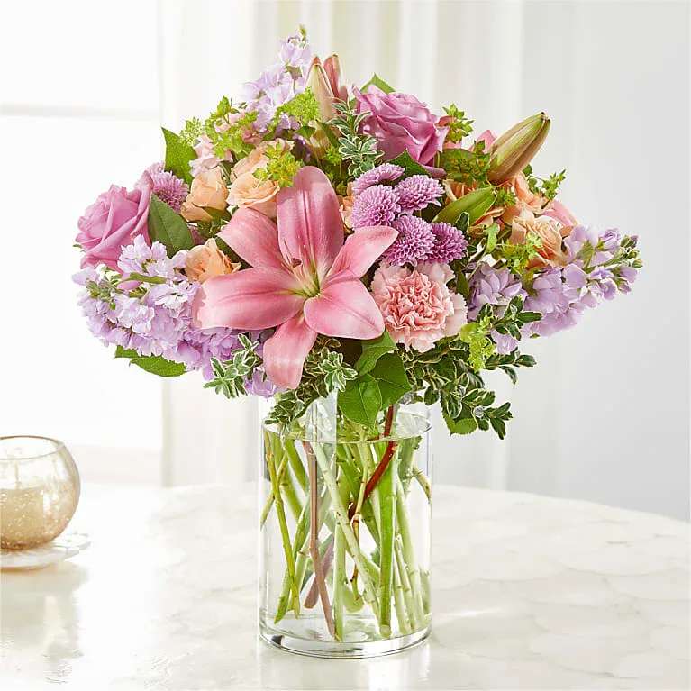 Pink lilies and mixed pastel flowers in a clear glass vase