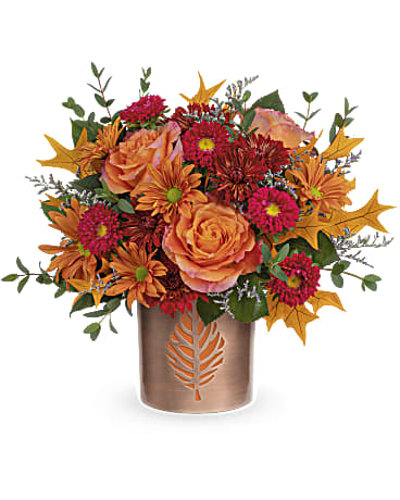  Leaves of Copper Bouquet - Nothing says fall like radiant orange roses and leaves in Teleflora's Leaves of Copper Bouquet. Fall flowers fill a shimmering copper-finished vase that can be enjoyed next fall with candlelight flickering through its delicate leaf cutout. Orange roses, red matsumoto asters, bronze cushion spray chrysanthemums and bronze daisy spray chrysanthemums are arranged with purple limonium and parvifolia eucalyptus. This autumn is delivered in Teleflora's Lovely Leaves Cylinder. Approximately 15 1/2" W x 13 1/2" H