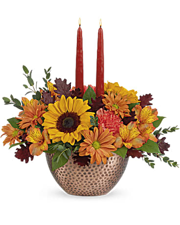Autumn Copper Centerpiece - With its shimmering, copper-hued bowl, radiant mix of sunflowers and glowing tapers, this stunning centerpiece celebrates the bountiful beauty of fall! This stunning centerpiece features medium yellow sunflowers, orange carnations, bronze daisy spray chrysanthemums, orange alstroemeria, parvifolia eucalyptus and lemon leaf, accented with preserved oak leaves and taper candles. Delivered in Teleflora's Copper Beauty bowl. Approximately 15 3/4" W x 15" H 
