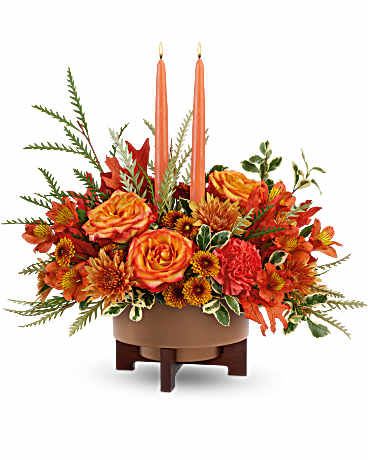 Fall Harvest Centerpiece - Warm hearts and tables with a Fall Harvest Centerpiece. Featuring two elegant taper candles and a rich mix of orange blooms, this stunning arrangement shines in a Modern Copper Planter. A perfect fit for Thanksgiving or any occasion this autumn. The Fall Harvest Centerpiece includes orange bi-color roses, orange alstroemeria, orange carnations, orange button spray chrysanthemums, and rust cushion spray chrysanthemums. Accented with grevillea, oregonia, preserved oak leaves, and two peach candles in Teleflora's Modern Copper planter Approximately 17 1/2" W x 11 1/2" H. 