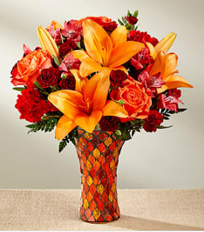 Autumn's Splendor - Saturated in the alluring hues of the harvest season, this fresh flower bouquet weaves together orange roses, burgundy mini carnations, red Peruvian Lilies, orange Asiatic Lilies, red carnations, orange spray roses, and lush greens to create a warm and inviting gift. Arranged beautifully within a keepsake stain glass inspired vase, capturing the eye with it's sparkle of gold and burgundy as it catches the light, this gorgeous fall bouquet is brought together for you to create an unforgettable thank you, happy birthday, or Thanksgiving gift.