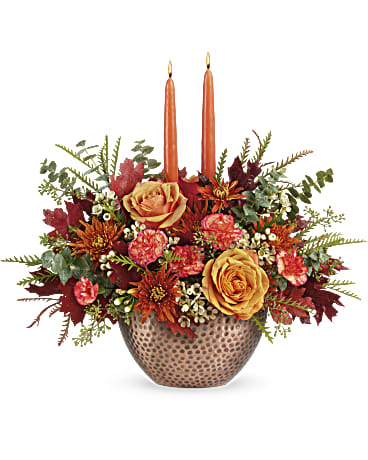 Gleaming Copper Centerpiece - Joyfully welcome the harvest season with this magnificent centerpiece of fall blooms and gleaming tapers, beautifully arranged in a hammered, copper-hued bowl that's sure to become a year-round décor favorite. This arrangement includes light orange roses, miniature orange carnations, bronze cushion spray chrysanthemums, white waxflower, spiral eucalyptus, grevillea and seeded eucalyptus, accented with transparent oak leaves and peach taper candles. Delivered in Teleflora's Copper Beauty bowl. Approximately 17 1/2" W x 15 1/2" H