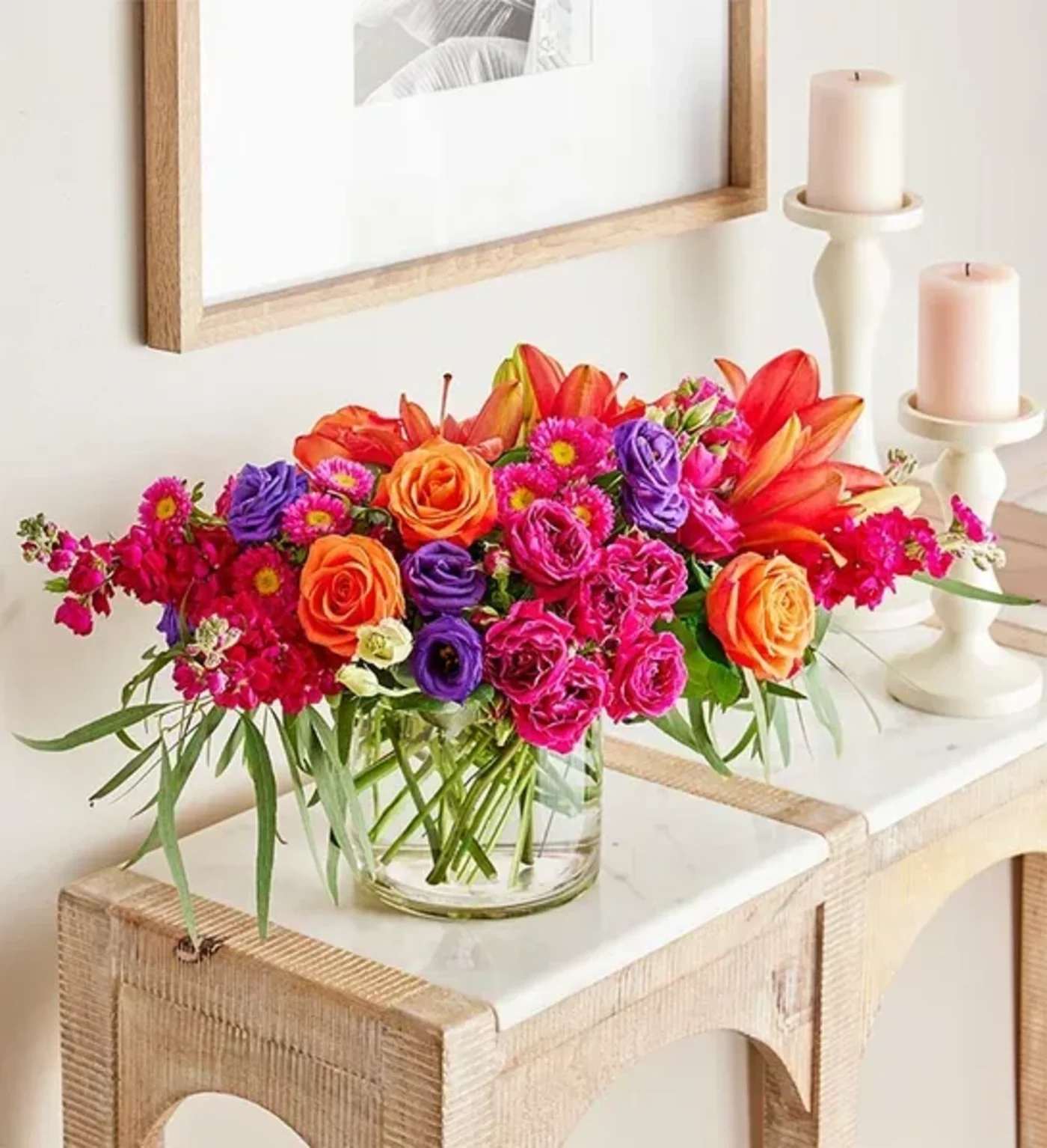 Bright mixed bouquet in a clear glass vase beside two candles