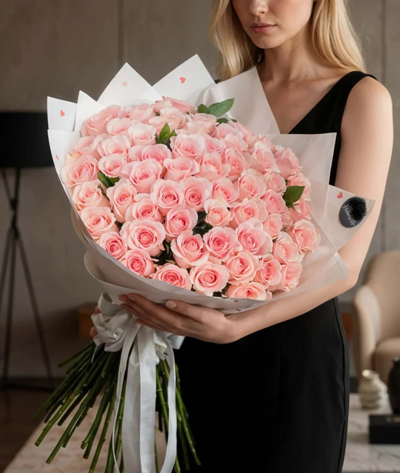 Woman holding a large bouquet of pale pink roses wrapped in white paper