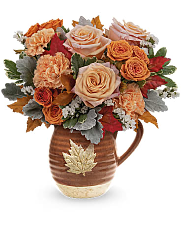 Golden Rose Bouquet - Nothing says fall quite like this bountiful bouquet of autumnal roses in an earthy glazed ceramic pitcher with falling leaf motif. This festive fall bouquet features peach roses, orange spray roses, orange carnations, white sinuata statice, dusty miller and variegated pittosporum accented with preserved oak leaves. The Golden Rose Bouquet is delivered in Teleflora's Cascading Blooms Pitcher. Approximately 13" W x 13 1/4" H