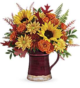Bounty Of Blooms Bouquet - This bright bouquet of seasonal sunflowers and roses is a joyful celebration of fall's bounty! Arranged in a stunning hand-glazed ceramic pitcher, it's a gift they'll enjoy for many autumns to come. Orange spray roses, medium yellow sunflowers, bronze cushion spray chrysanthemums, and bronze daisy spray chrysanthemums are arranged with sword fern, huckleberry, grevillea, and rust preserved oak leaves. Delivered in a Fields of Fall Pitcher. Approximately 14 1/2" W x 14" H