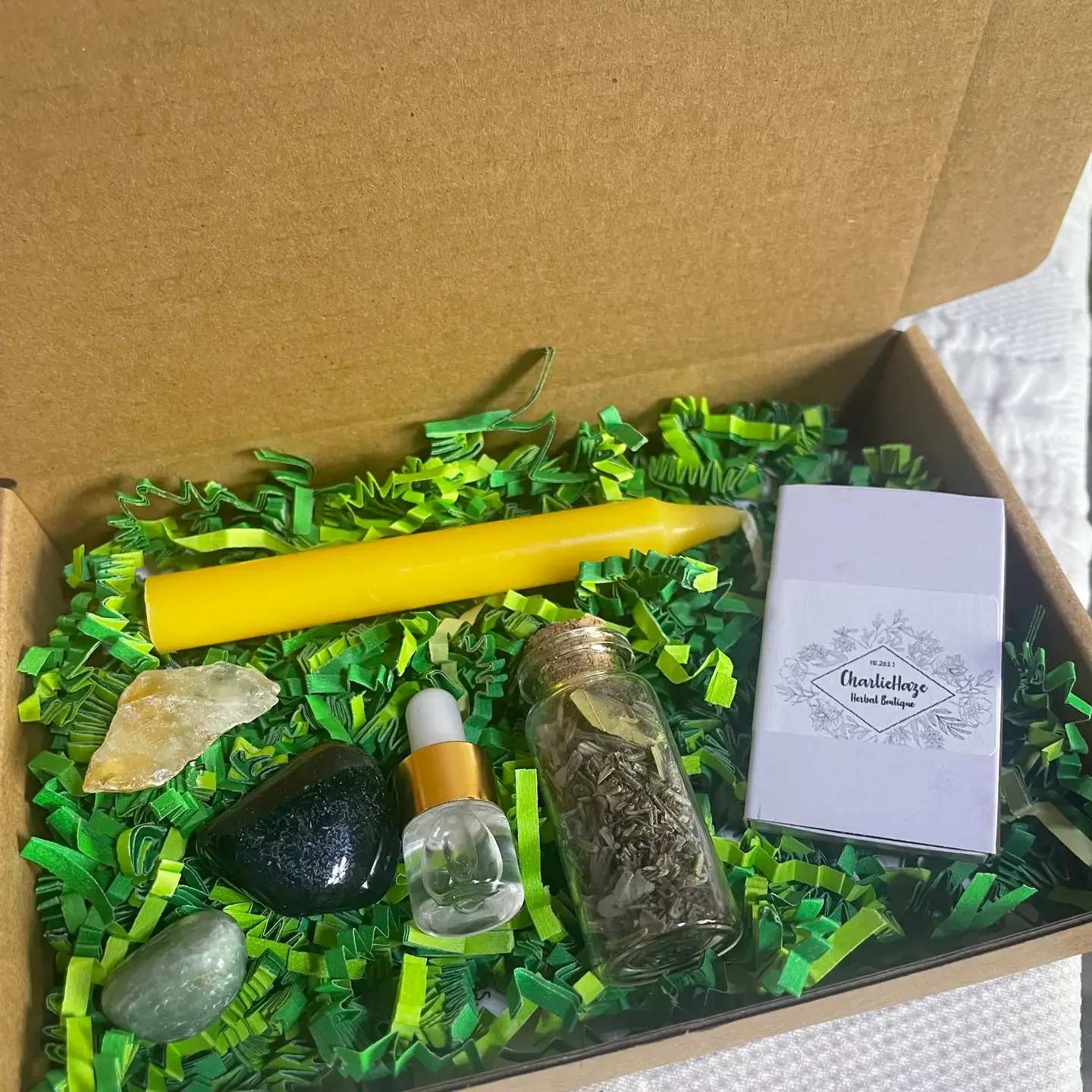 Gift box with a yellow candle, crystals, a dropper bottle, and a small herb vial