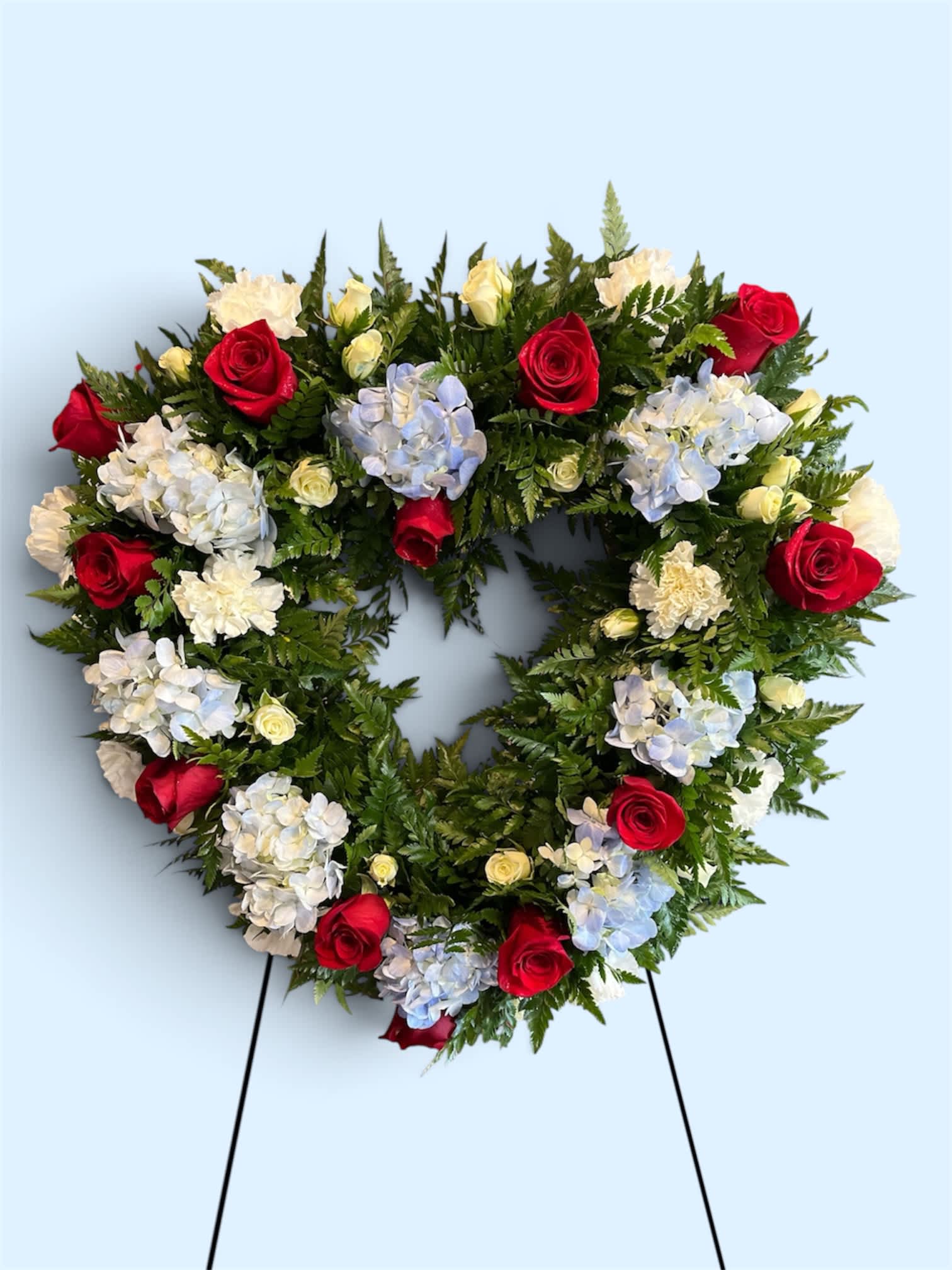 Heart-shaped floral wreath with red roses and pale hydrangeas on a stand