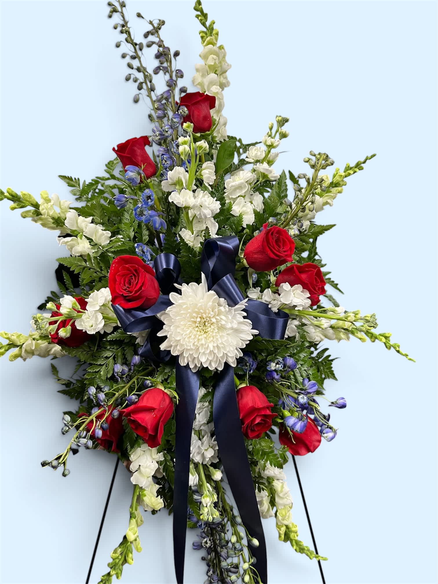 Standing floral spray with red roses, white blooms, and a navy ribbon