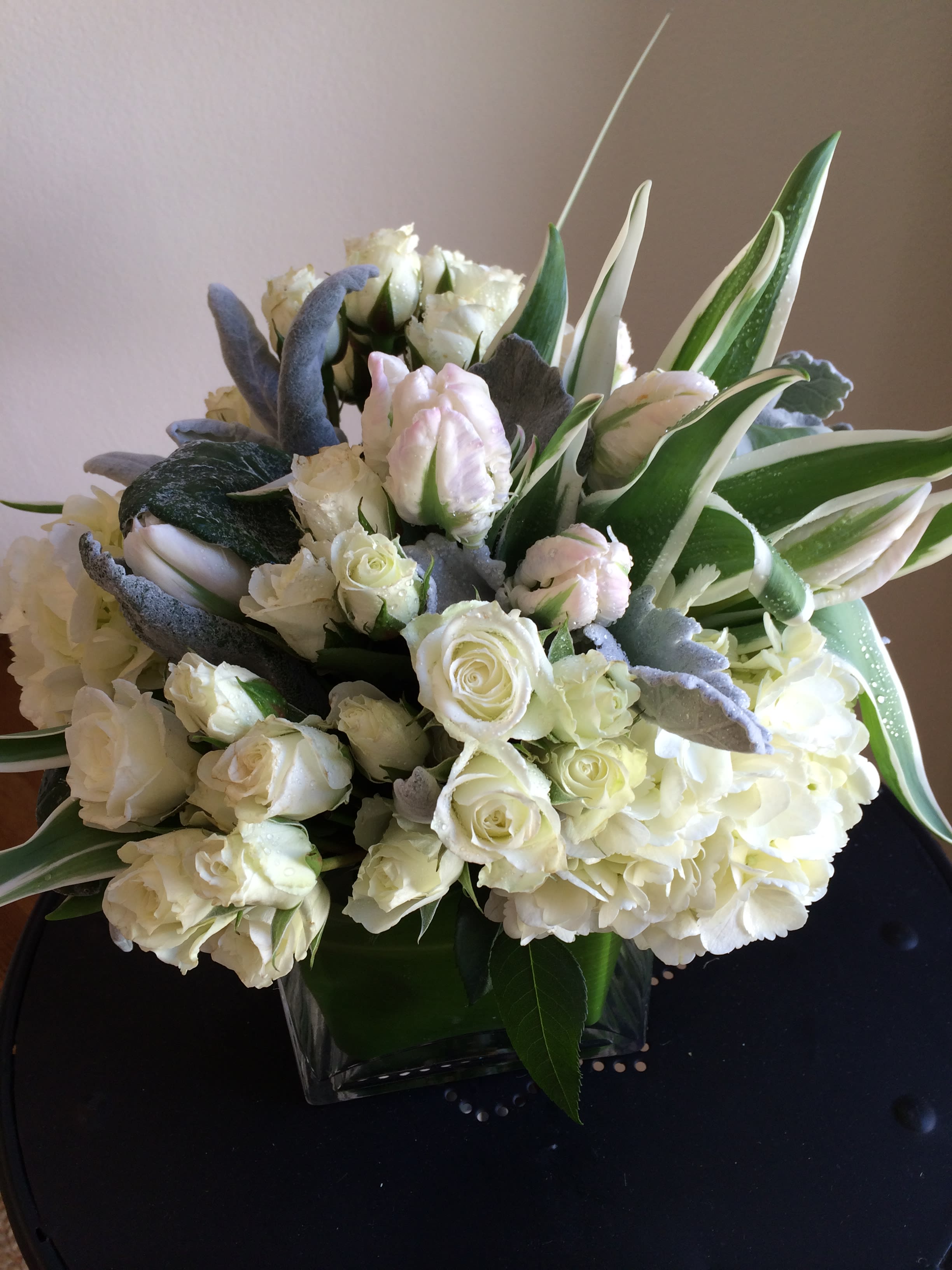 White roses and hydrangeas in a square glass vase with variegated leaves