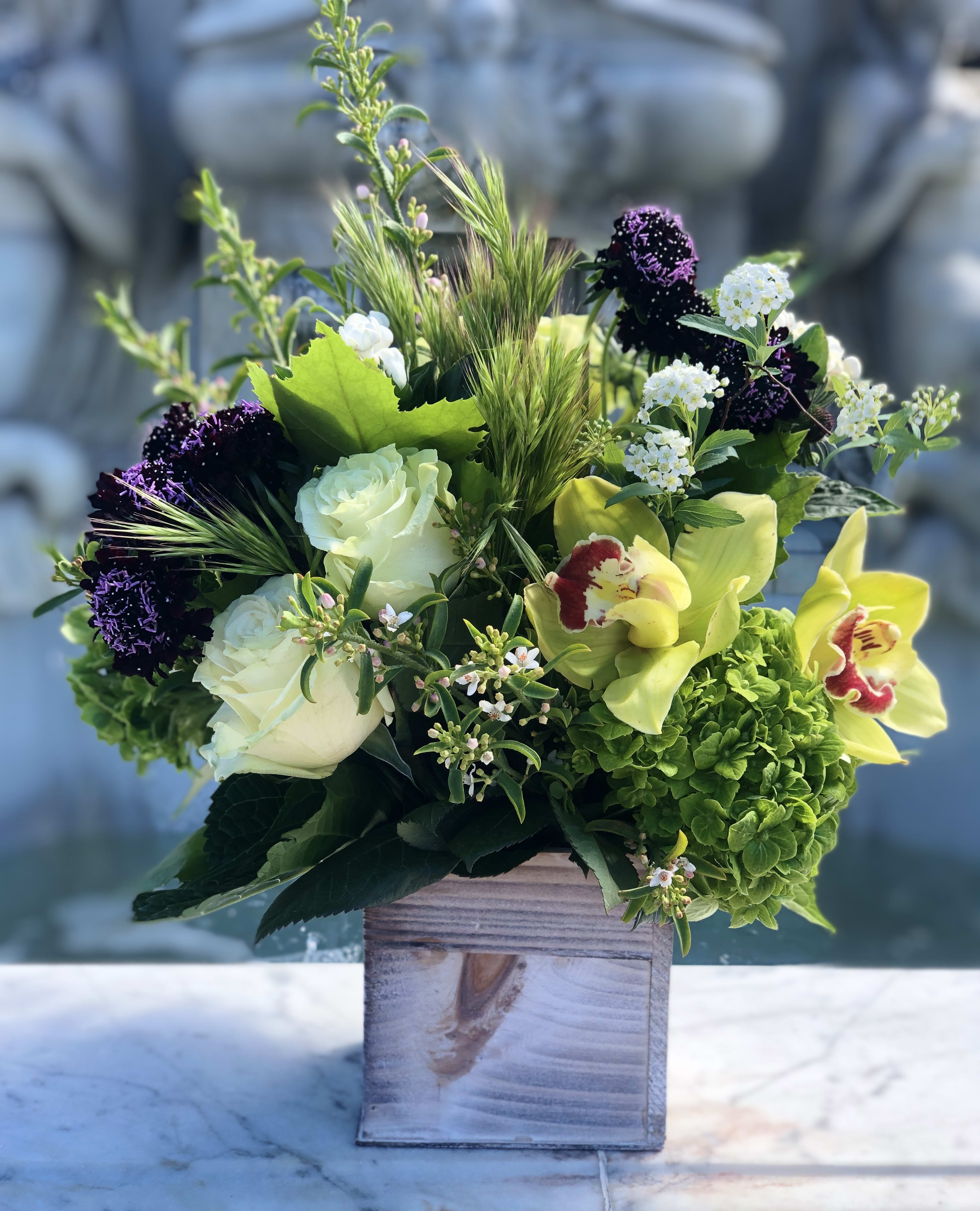 Arrangement of green hydrangea, white roses, and yellow orchids in a rustic wooden cube vase